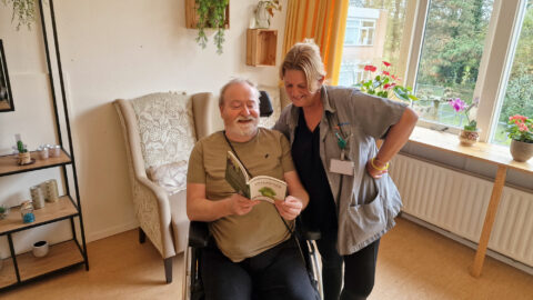 Gastvrouw/zorgmedewerker Suzan van der Weurf van Woonzorgcentrum Hof van Sloten en Joe Stack met het cadeauboek 'Natuur met een knipoog', Gefladder deel 1